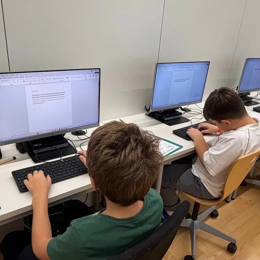 Vier Kinder sitzen an einem Schreibtisch mit Computern. Sie tippen auf ihren Tastaturen.