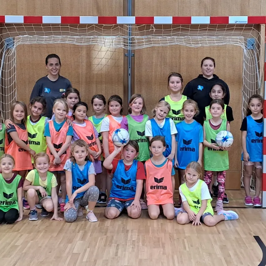 Eine Gruppe von Kindern in passenden Uniformen posiert für ein Foto vor einem Tor in einer Turnhalle.