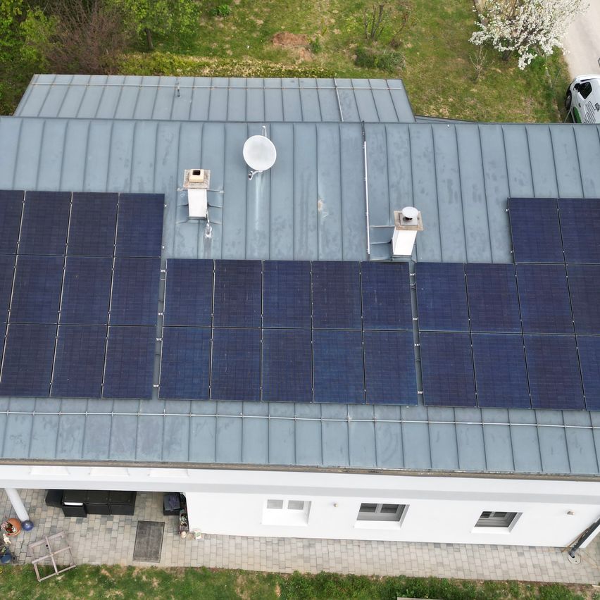 Eine Luftaufnahme eines Hauses mit Solarpanelen auf dem Dach. Die Panele sind ordentlich angeordnet, und das Haus hat eine weiße Außenfassade.