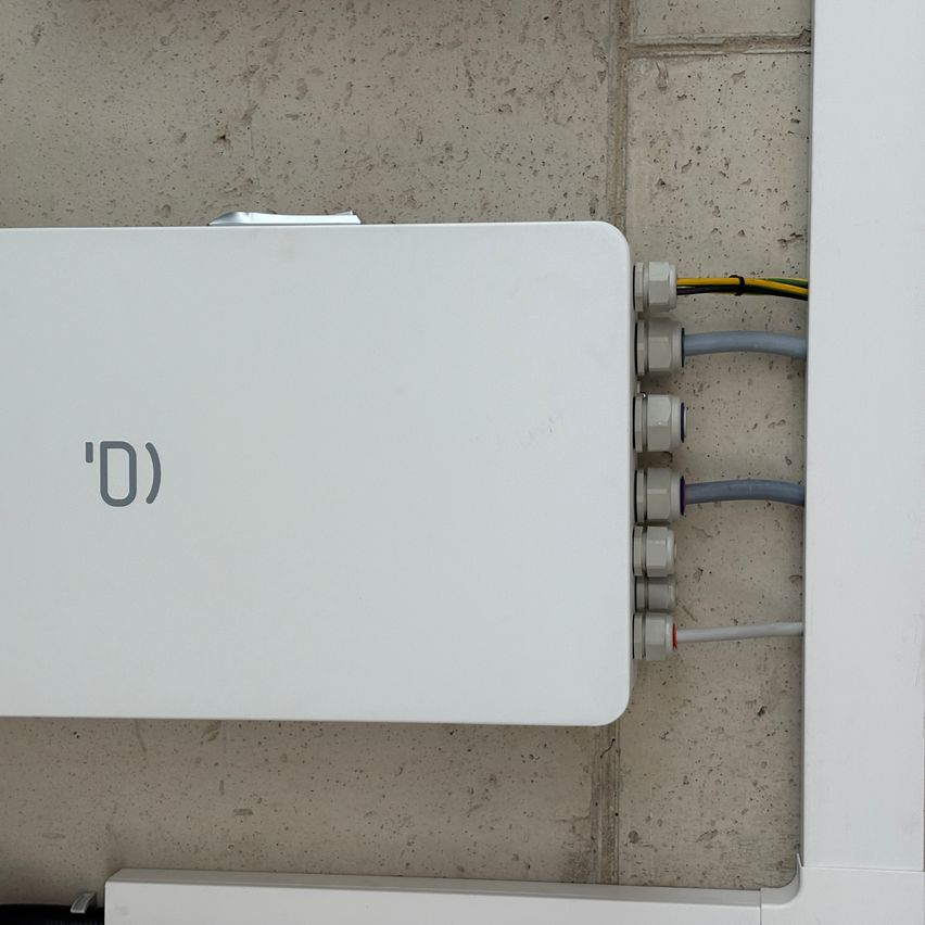 Ein weißer Kasten mit 'D' darauf ist an einer Wand montiert. Mehrere Drähte sind mit dem Kasten verbunden.