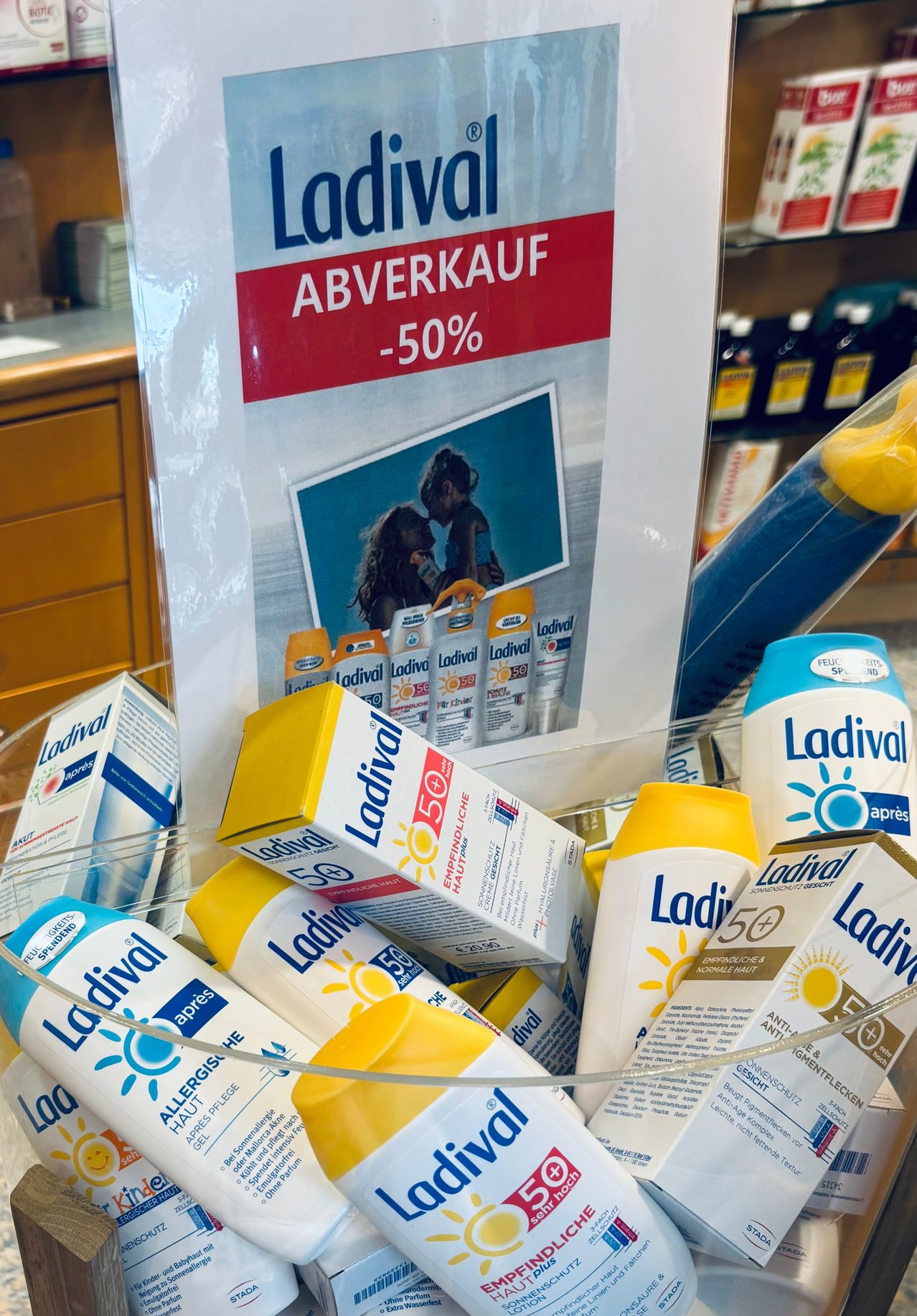 Eine Anzeige von Ladival-Sonnenschutzprodukten im Angebot mit 50% Rabatt, gezeigt in einem Geschäft mit verwischtem Hintergrund. Die Produkte sind in verschiedenen Farben und Größen und das Schild darüber zeigt den Verkauf an.
