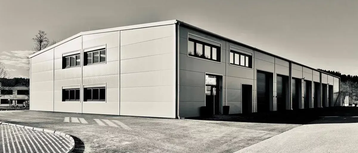 Ein monochromes Bild eines großen, modernen Gebäudes mit mehreren Fenstern und mehreren Garagentoren davor. Das Gebäude hat ein flaches Dach und ist von einem leeren Parkplatz umgeben.