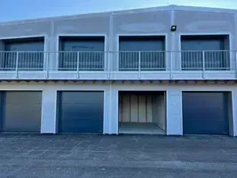 Ein modernes Gebäude mit vier Garagen, einem Balkon und einer Lampe auf dem Dach. Die Garagen haben graue Türen und befinden sich auf zwei Ebenen.