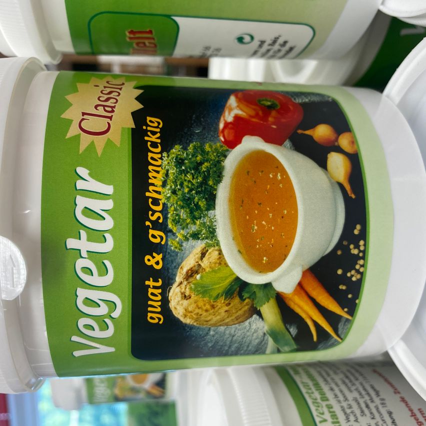 Ein Behälter mit 'Vegetar Classic' Suppenmischung, die eine Illustration einer Suppenschüssel mit Gemüse wie Karotten, Petersilie und Zwiebeln zeigt. Das Etikett ist grün und weiß.