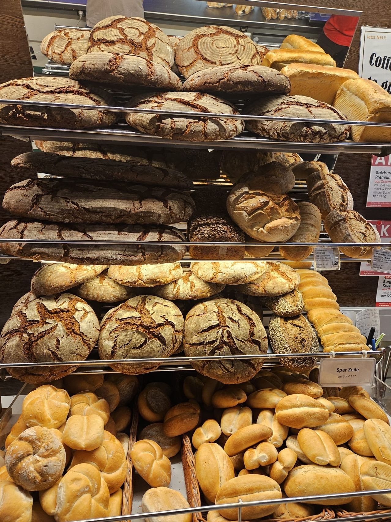 A display of various types of bread, including rye, sourdough, and others, arranged on multiple shelves in a bakery.