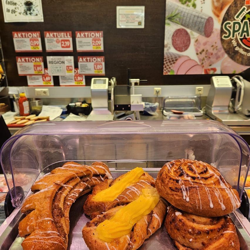 A display case with various pastries, including cinnamon rolls with yellow filling and a spiral roll with icing, in a bakery or cafe setting.