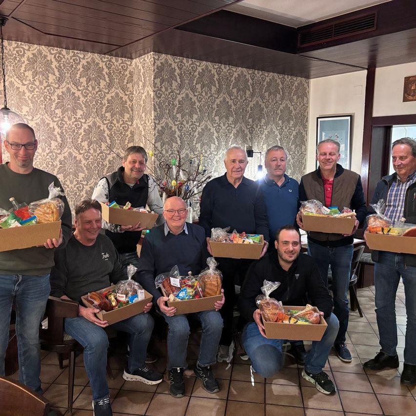 Eine Gruppe von Männern, alle lächelnd, halten Boxen mit Essen und stehen zusammen in einem Innenbereich.