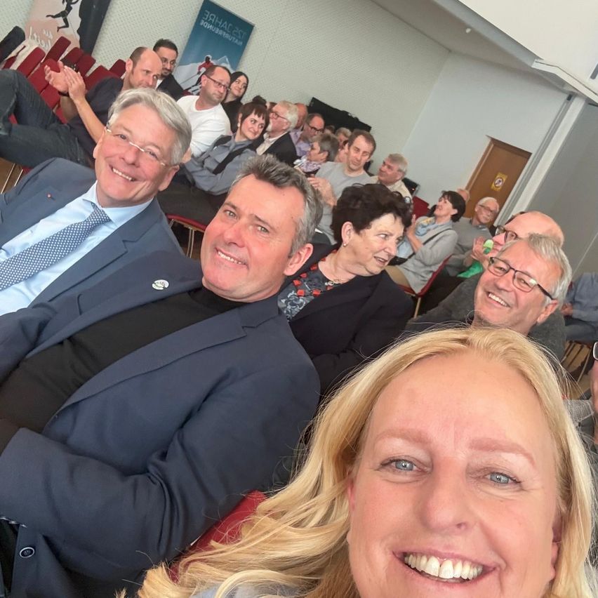 Eine Gruppe von Menschen, darunter zwei Männer und zwei Frauen, lächelt und posiert für ein Foto in einem Raum.