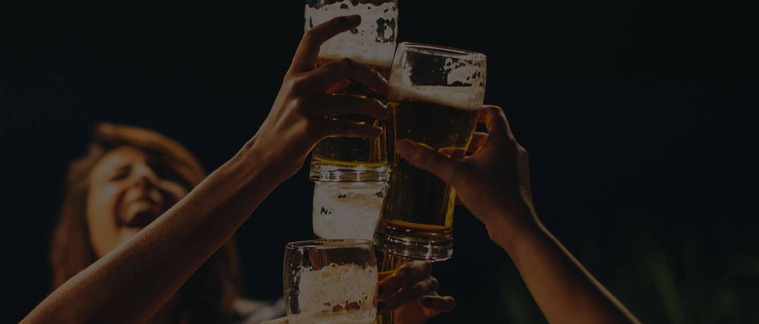 Mehrere Hände halten Gläser mit Bier, die aufeinandergestapelt sind. Die Gläser sind mit schaumiger, goldener Flüssigkeit gefüllt.