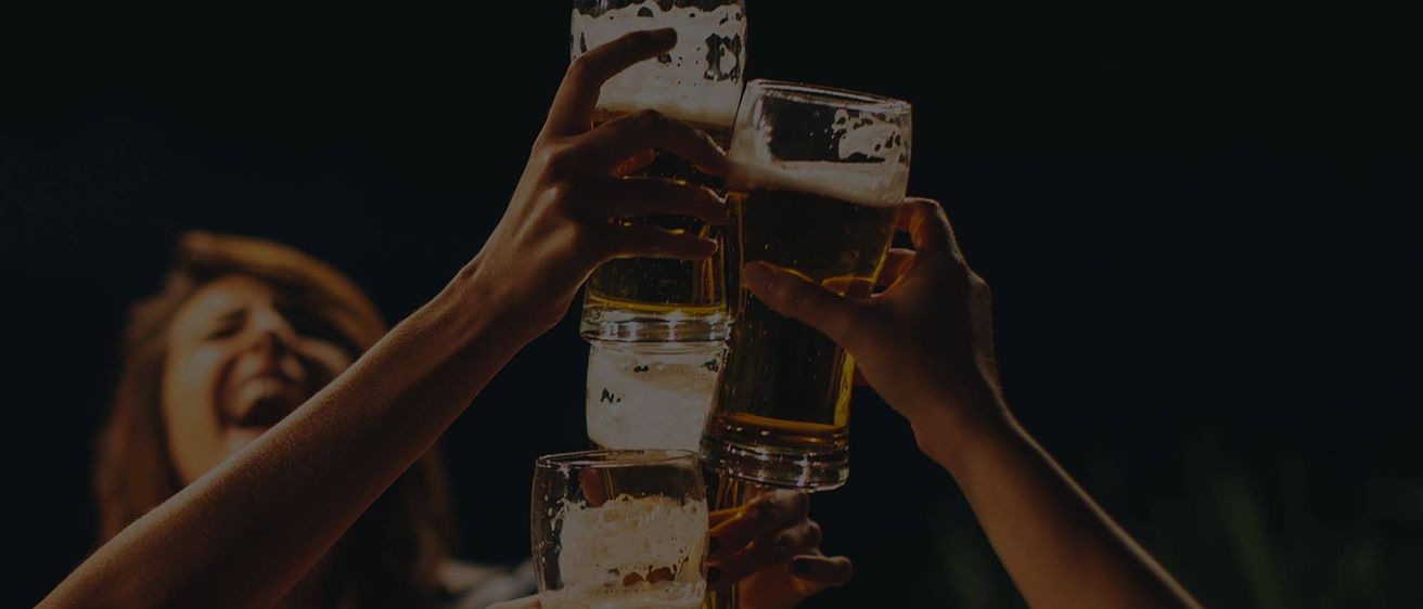 Mehrere Hände halten Gläser mit Bier, die aufeinandergestapelt sind. Die Gläser sind mit schaumiger, goldener Flüssigkeit gefüllt.