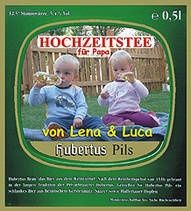 Eine Werbung für Hochzeitstee für Papa mit zwei Babys, die auf dem Gras sitzen. Ein Baby hält eine Flasche und das andere einen Spielzeug. Der Text lautet 'von Lena & Luca Hubertus Pils.' Der Hintergrund zeigt einen Zaun und Grünpflanzen.