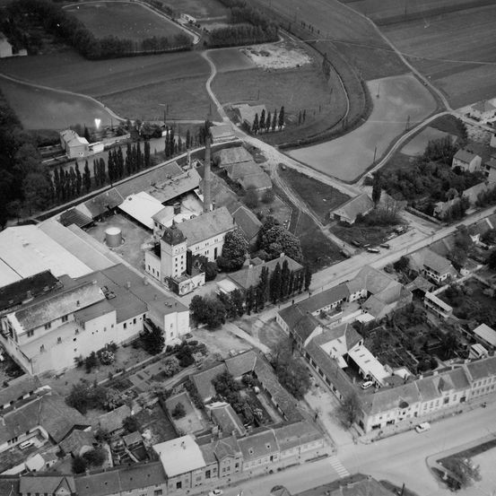 Ein Luftbild einer kleinen Stadt mit mehreren Gebäuden, Straßen und Bäumen. Die Stadt ist von weitläufigen Ackerflächen umgeben.