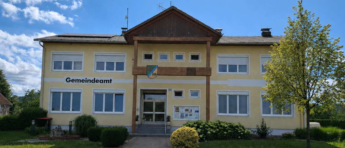 Ein gelbes Gebäude mit dem Namen Gemeindeamt auf der Vorderseite, mit Fenstern und einem Weg, der zum Eingang führt.