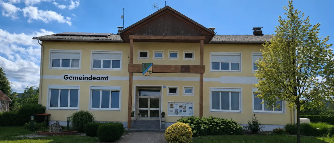 Ein gelbes Gebäude mit dem Namen Gemeindeamt auf der Vorderseite, mit Fenstern und einem Weg, der zum Eingang führt.