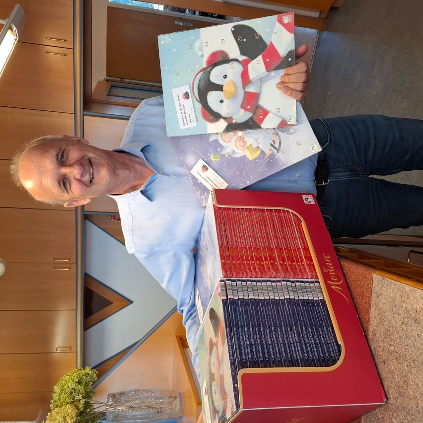 Ein Mann hält ein Buch mit einem Pinguin und eine Bücherkiste hoch.