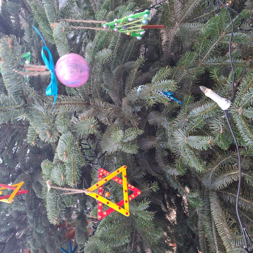 Ein geschmückter Weihnachtsbaum mit verschiedenen Ornamenten und bunten Dekorationen, darunter eine lila Kugel und ein gelber Stern.