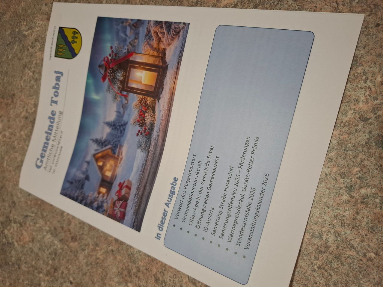 Eine Karte mit dem Titel 'in dieser Ausgabe' zeigt eine Winterszene mit einer Laterne, Bäumen und einem Haus. Der Hintergrund ist verschneit. Die Karte listet verschiedene Dienste auf, darunter eine App, Ausweiskarten, Straßennamen und Veranstaltungen. Die Karte stammt von einer Gemeinde und enthält ein Bild einer Weihnachtslaterne.