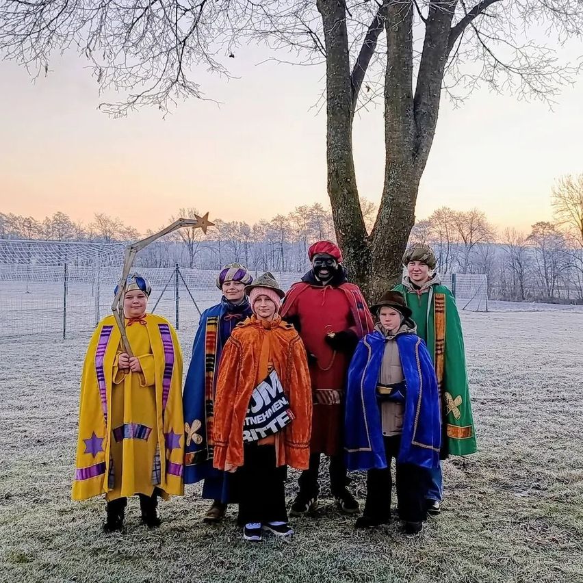 Eine Gruppe von Kindern in Kostümen posiert für ein Foto auf einem verschneiten Feld mit einem Baum im Hintergrund.