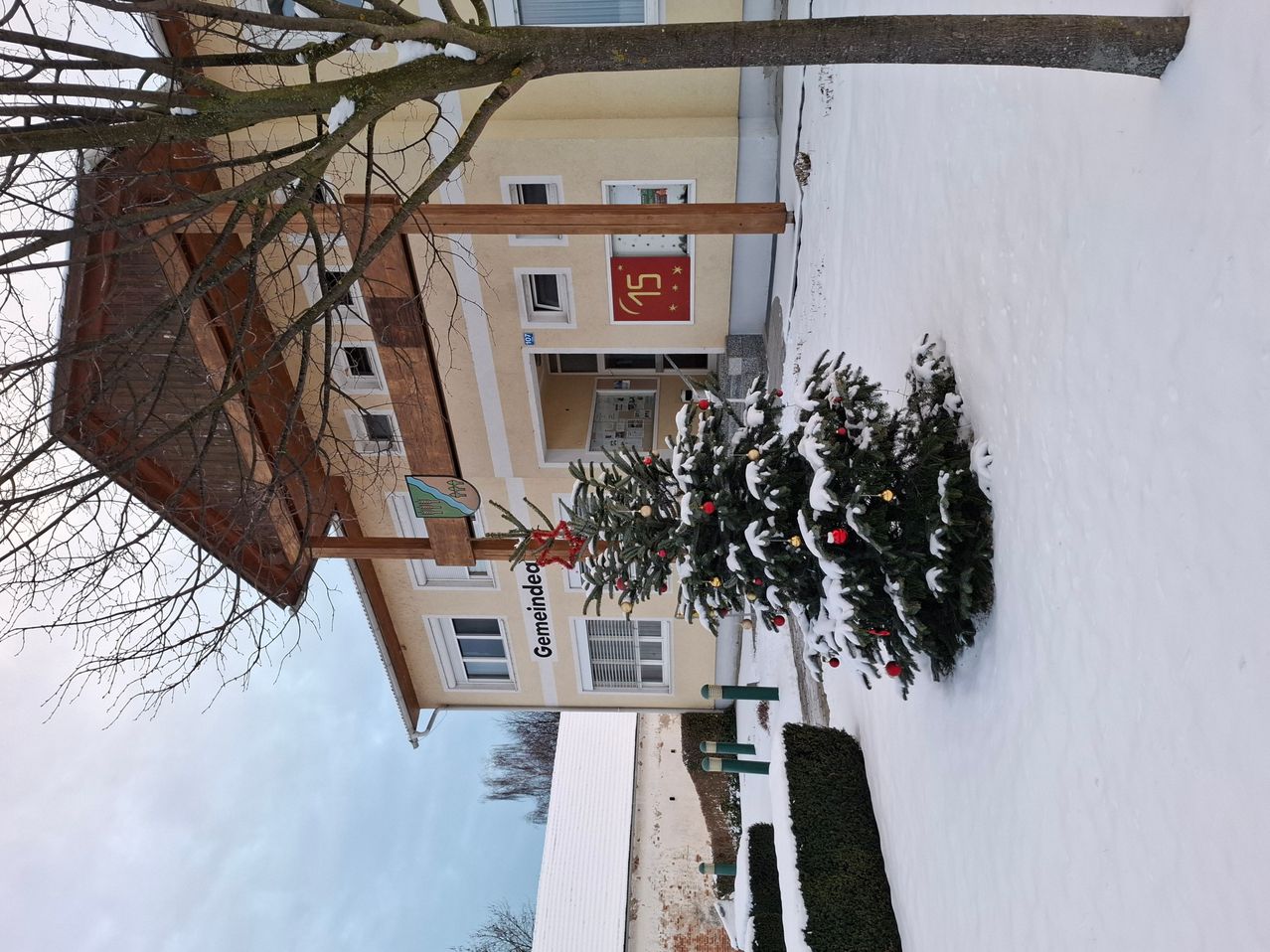 Luftaufnahme eines Gebäudes mit einem mit Schnee bedeckten Weihnachtsbaum davor. Das Gebäude hat ein rotes Schild mit der Nummer 15.