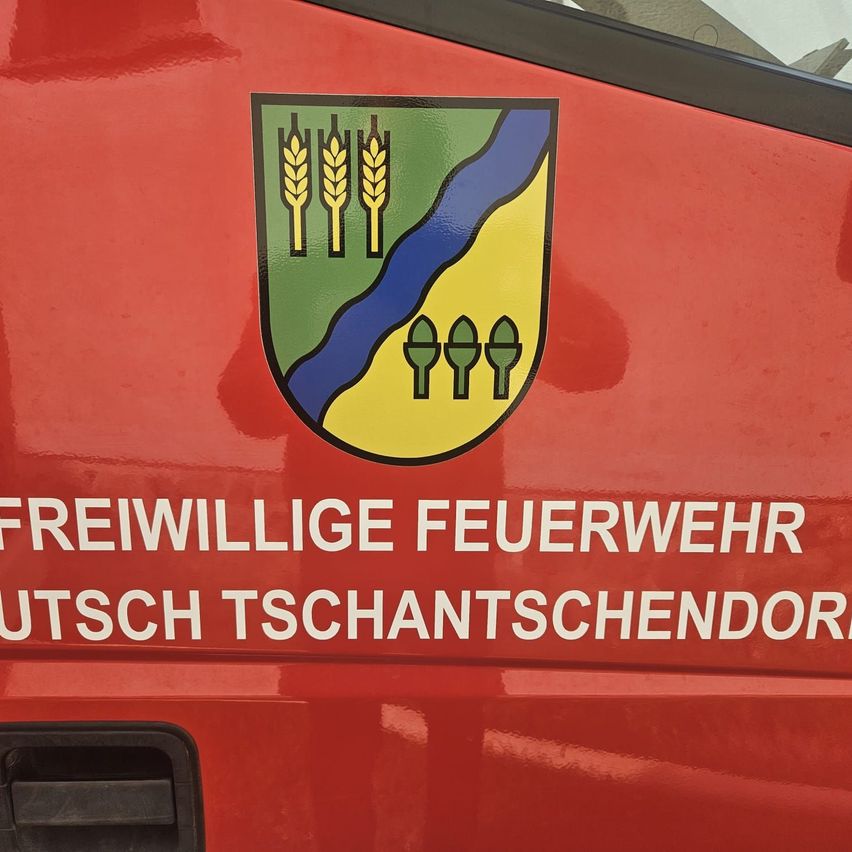 Ein rotes Fahrzeug mit einem Logo, das Weizen, Wasser und Bäume zeigt, und den Worten 'Freiwillige Feuerwehr' und 'Deutsch Tschantschendor'.