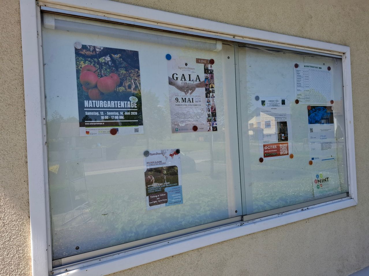Ein Anschlagbrett mit verschiedenen Plakaten. Ein Plakat handelt von einem Naturgarten-Event. Ein anderes Plakat sagt 'GALA' mit Datum und Ort.