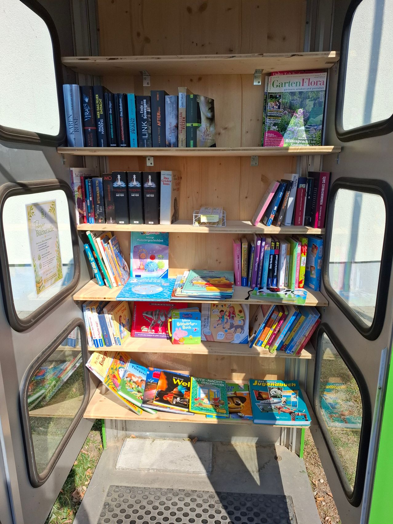 Ein hölzerne Bücherregal in einem Bus, gefüllt mit Büchern und Zeitschriften, einschließlich einer Zeitschrift mit dem Titel Garten Flora.
