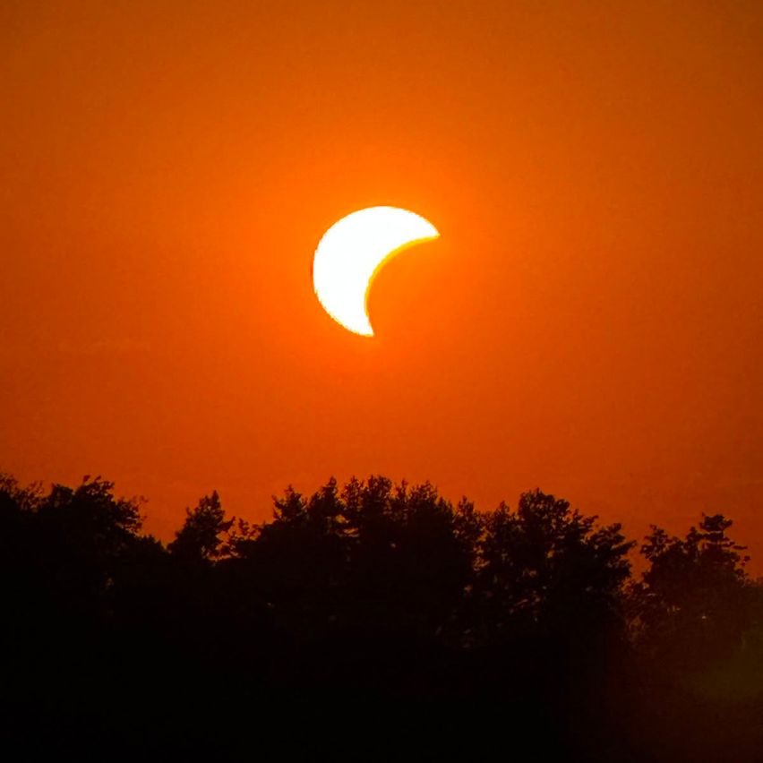 Ein partieller Sonnenfinsternis, bei dem die Sonne teilweise durch den Mond verdeckt wird, vor einem feurig orangefarbenen Himmel.