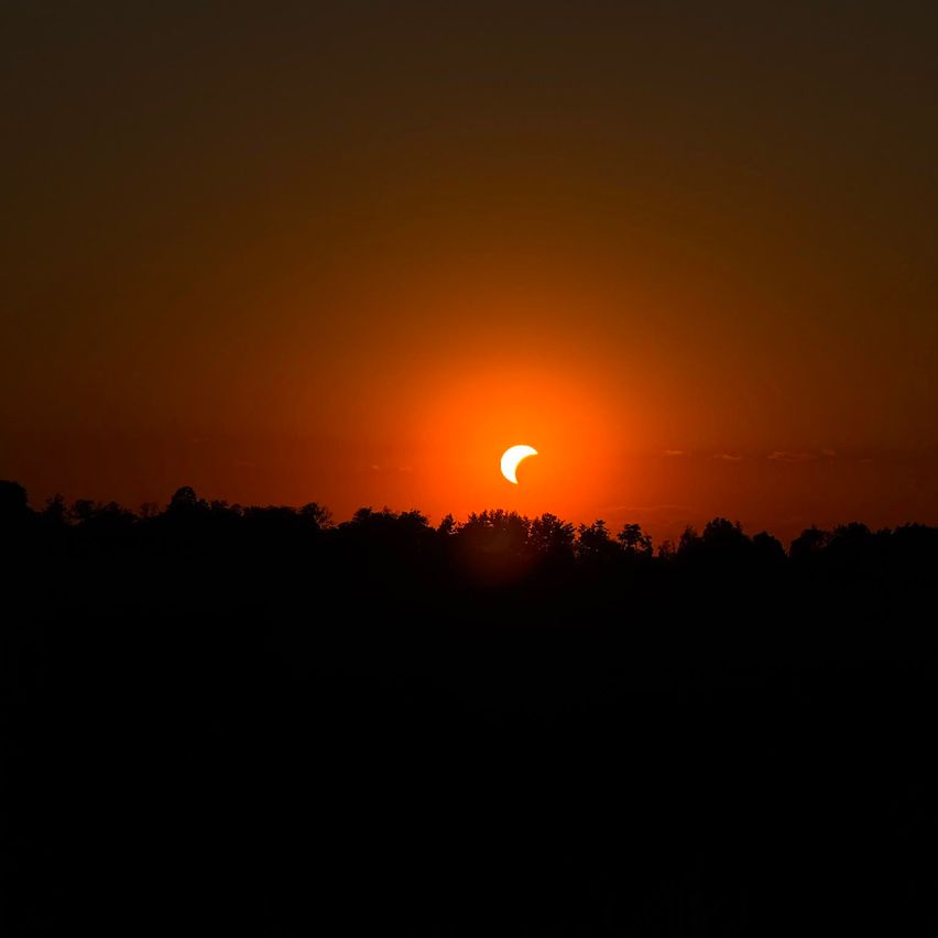Ein teilweiser Sonnenfinsternis bei Sonnenuntergang, wobei der Mond die Sonne teilweise bedeckt und eine dramatische Silhouette über der Landschaft wirft.