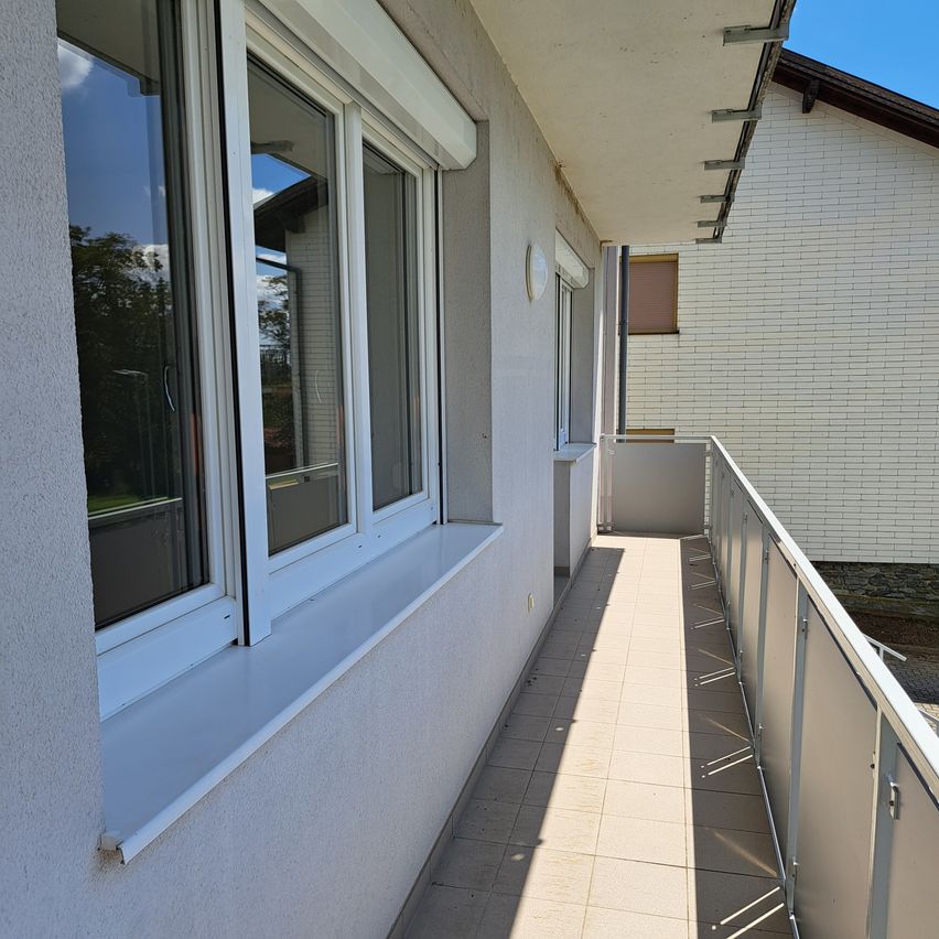 Ein Balkon mit weißen Wänden und Fenstern, der zu einem gefliesten Boden führt. Ein Fenstersims mit einem weißen Rand ist sichtbar.