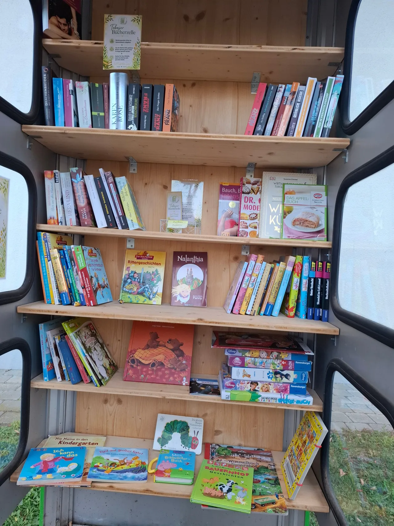 Ein hölzerne Bücherregal gefüllt mit Kinderbüchern und Zeitschriften ist in einem Bus.