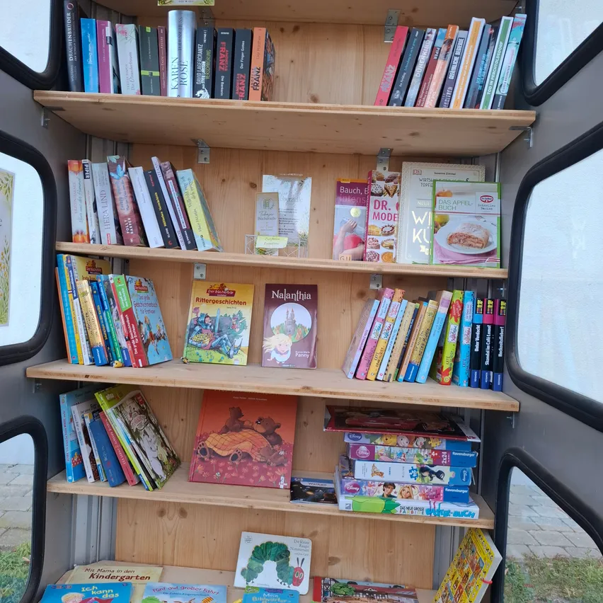 Ein hölzerne Bücherregal gefüllt mit Kinderbüchern und Zeitschriften ist in einem Bus.