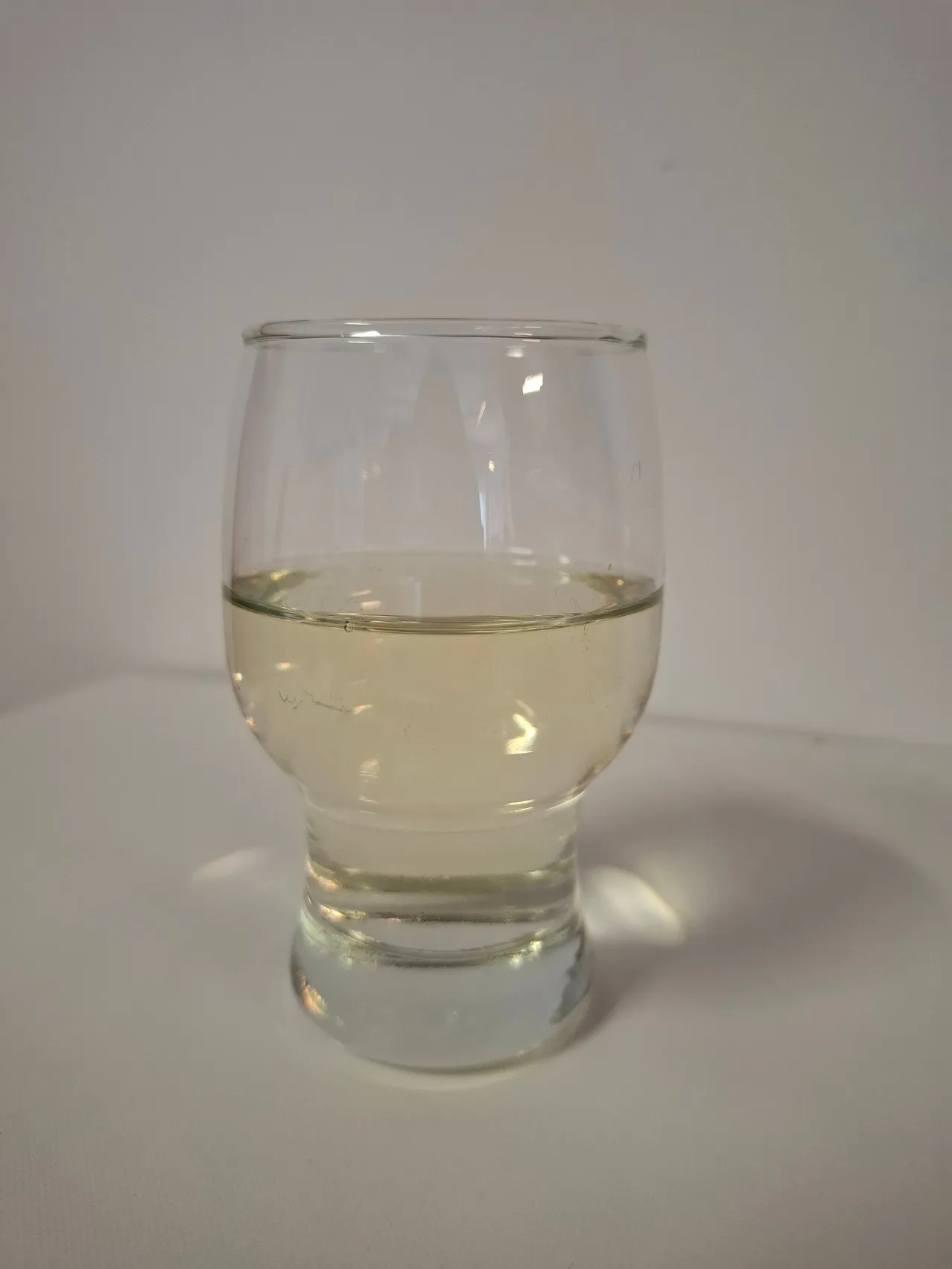 Ein klares Glas mit einer hellgelben Flüssigkeit auf einer weißen Oberfläche.