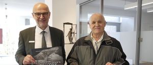 Zwei Männer halten ein Buch und ein Schild. Das Buch heißt Schellenberger Eishohle. Das Schild sagt Gemeinsam ist einfach. 2.000,- €. Dahinter ist eine Glaswand und eine Skulptur.