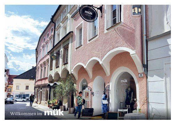 A street scene with a storefront named 'muk' with a woman walking past, a parked car, and a person standing outside.