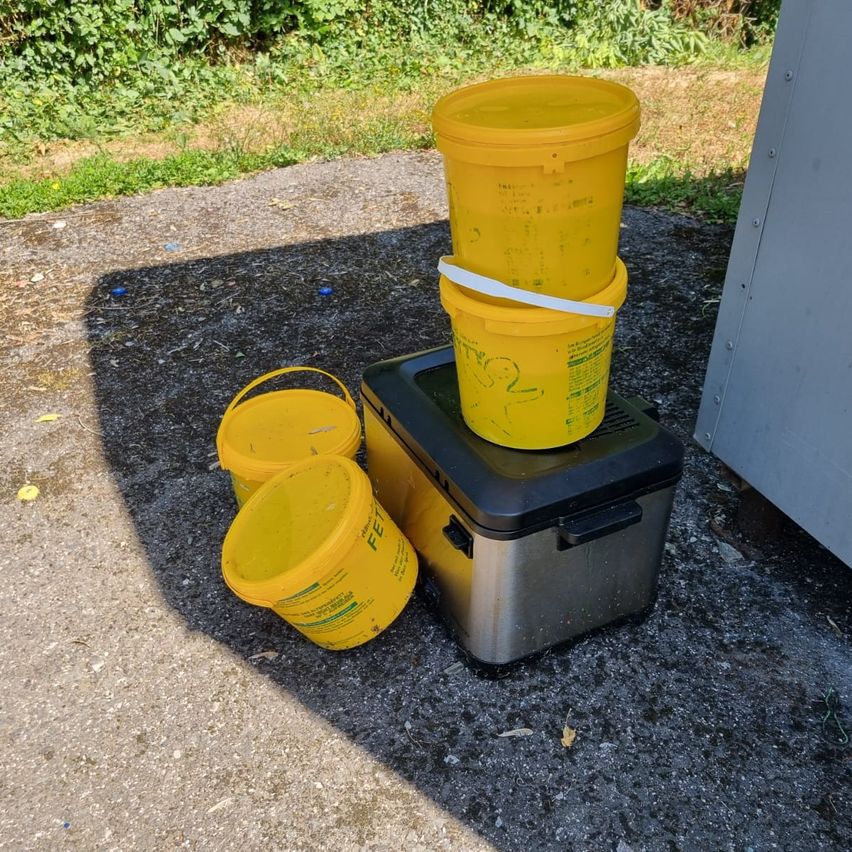 Drei gelbe Eimer sind auf einem Kühler mit schwarzem Deckel gestapelt. Die Eimer sind wahrscheinlich zum Sammeln von Wasser gedacht.