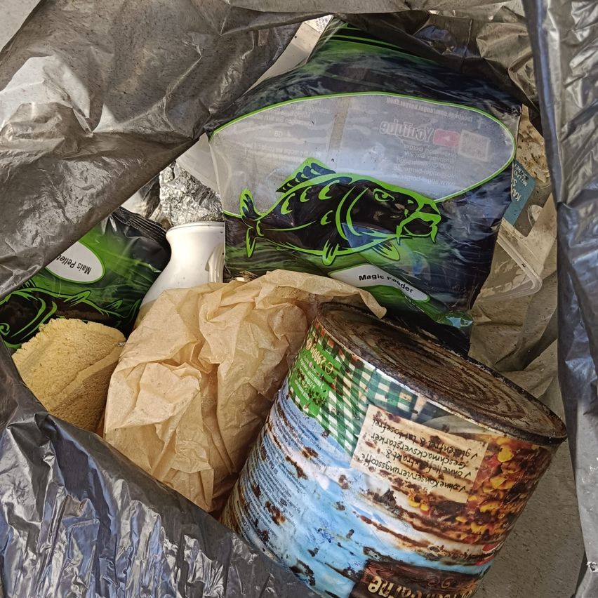 Ein Plastikbeutel mit einem Fischbeutel, einem Glas, einem Papierbeutel und einer Lebensmitteldose. Der Fischbeutel sagt 'Magic feeder' und die Dose hat ein Etikett mit fremdsprachigem Text.