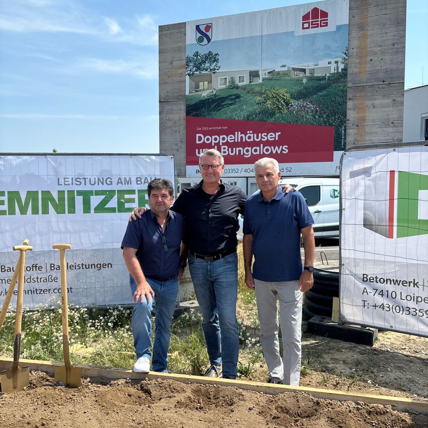 Drei Männer stehen vor einer Baustelle mit Schaufeln, Bannern und einem Van. Ein Banner steht für 'Doppelhauser Bungalows'.