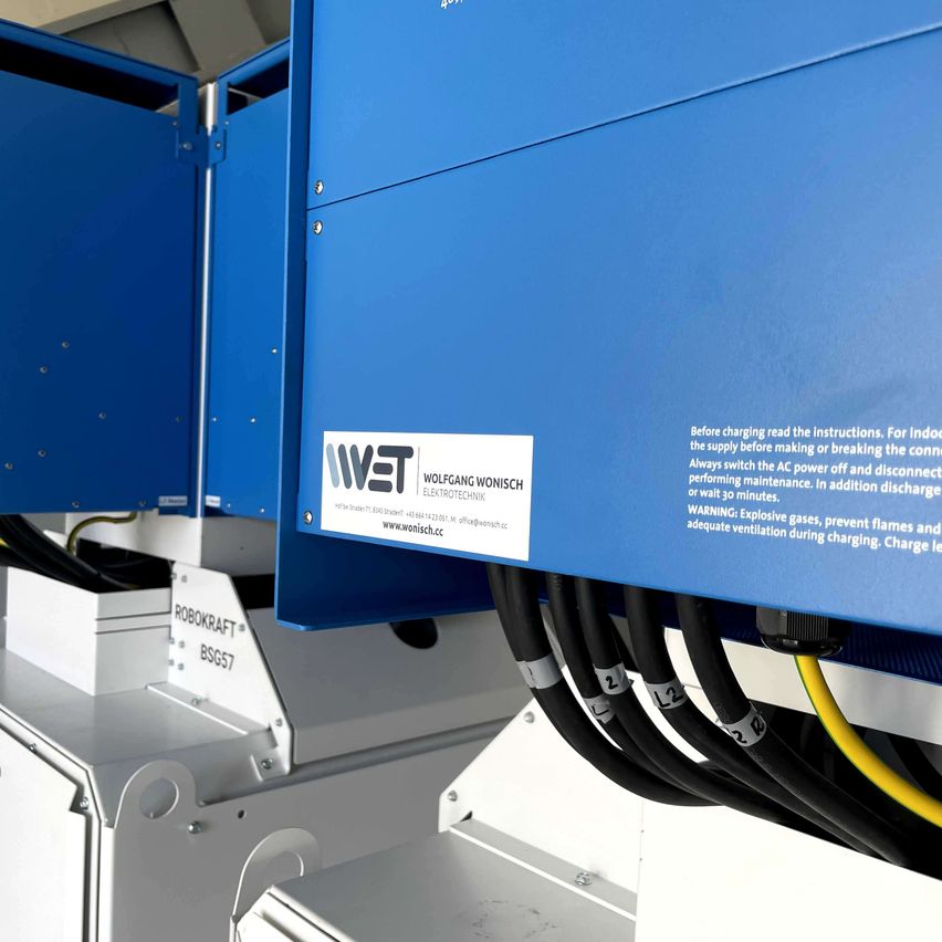 Nahaufnahme eines elektrischen Bauteils mit einem Label, 'WET', in einer Fabrikumgebung. Darunter befindet sich ein Warnhinweis, der lautet: 'Vor dem Laden die Anweisungen lesen.'