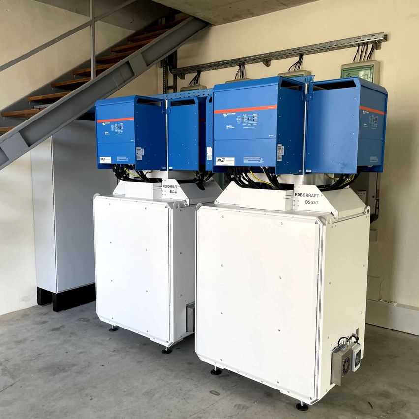 Drei blaue und weiße elektrische Geräte sind in einem Raum gestapelt. An jedem Gerät sind mehrere Kabel angeschlossen. Die Geräte stehen auf einem Betonboden.
