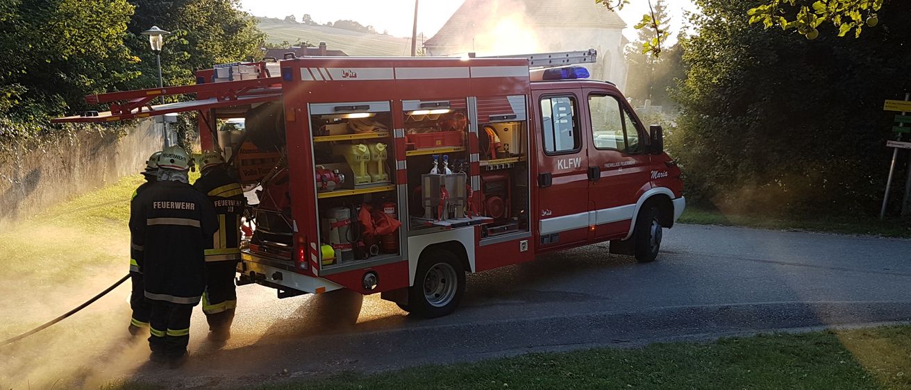 Zwei Feuerwehrleute sprühen Wasser aus einem roten Feuerwehrauto, wahrscheinlich während einer Brandübung oder Ausbildung.