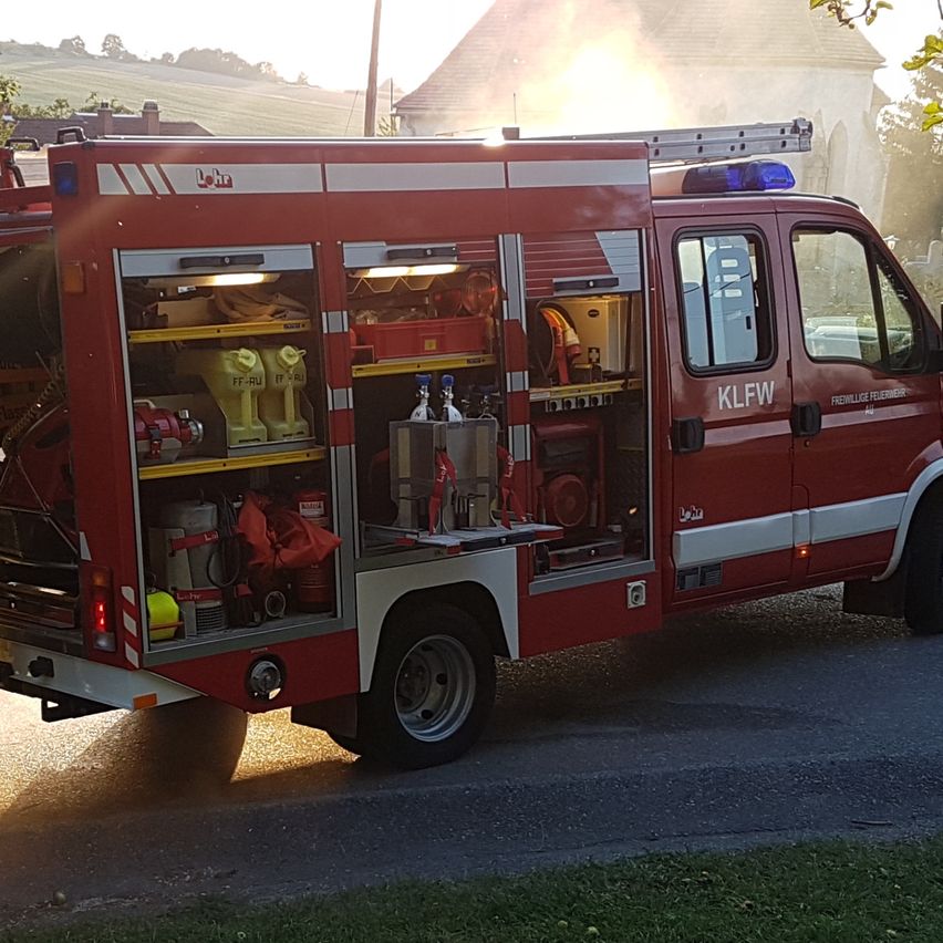 Zwei Feuerwehrleute sprühen Wasser aus einem roten Feuerwehrauto, wahrscheinlich während einer Brandübung oder Ausbildung.
