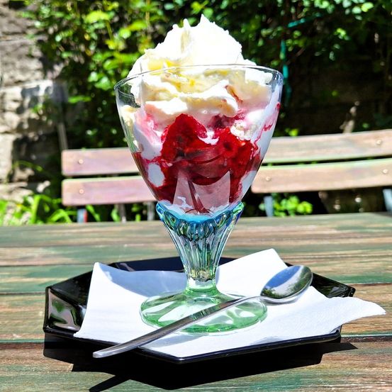 Ein Dessertglas mit Erdbeereis, Schlagsahne und einem Löffel auf einem schwarzen Teller mit einer weißen Serviette.