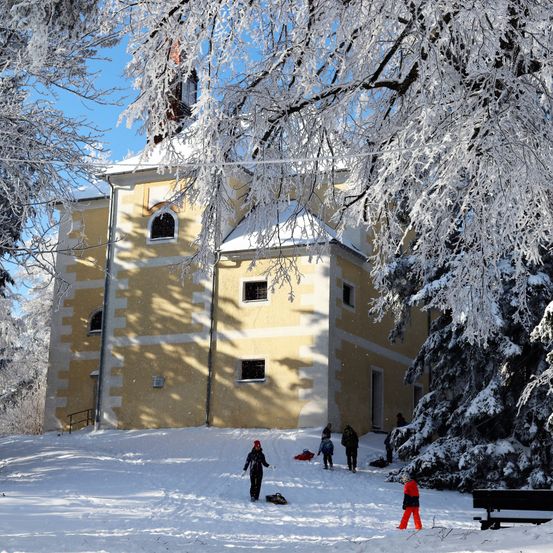 Einige Leute spielen im Schnee vor einer schneebedeckten Kirche.