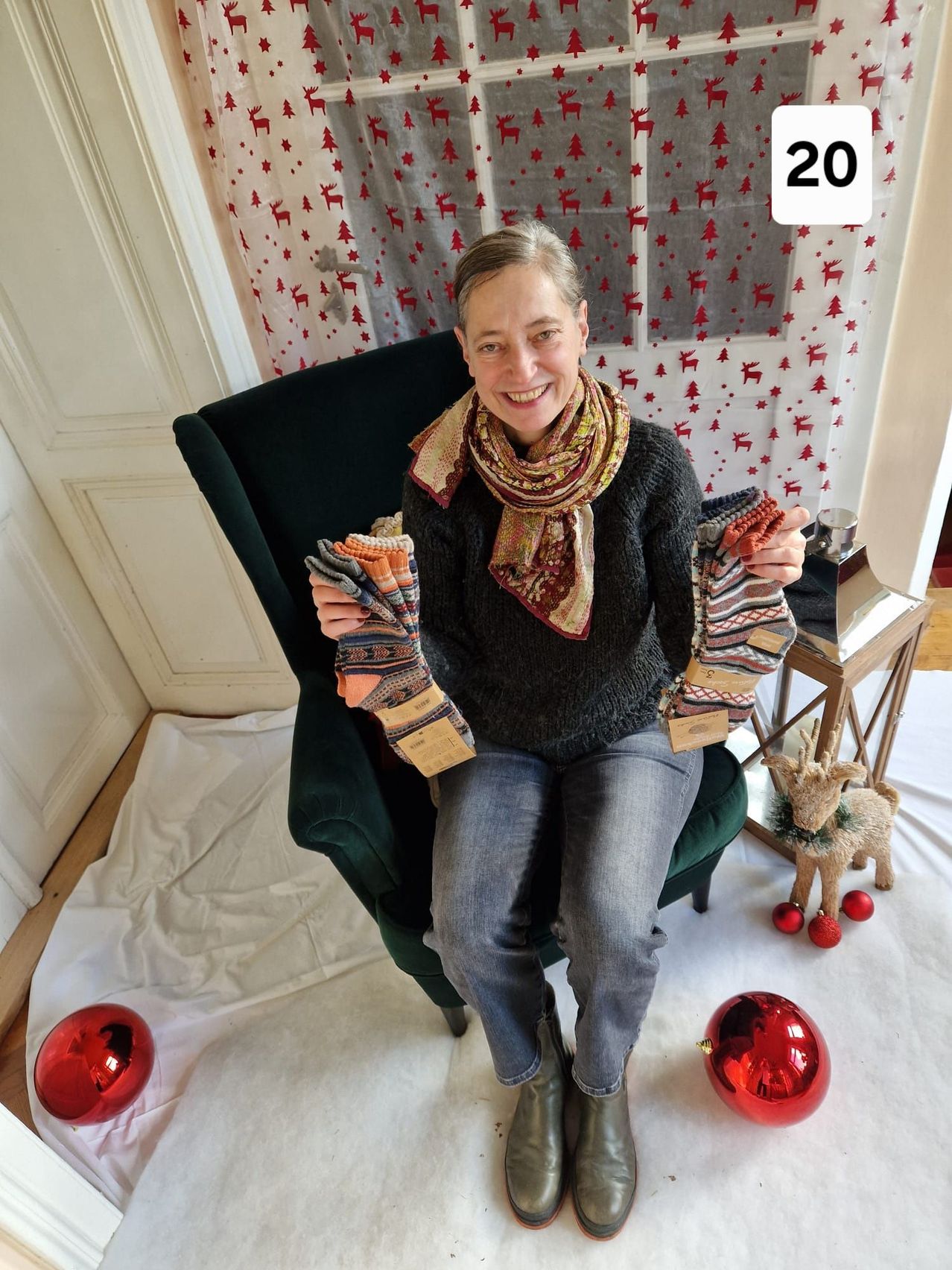 Eine Frau sitzt auf einem grünen Stuhl und hält ein Paar Socken hoch. Sie lächelt und scheint für ein Foto zu posieren.