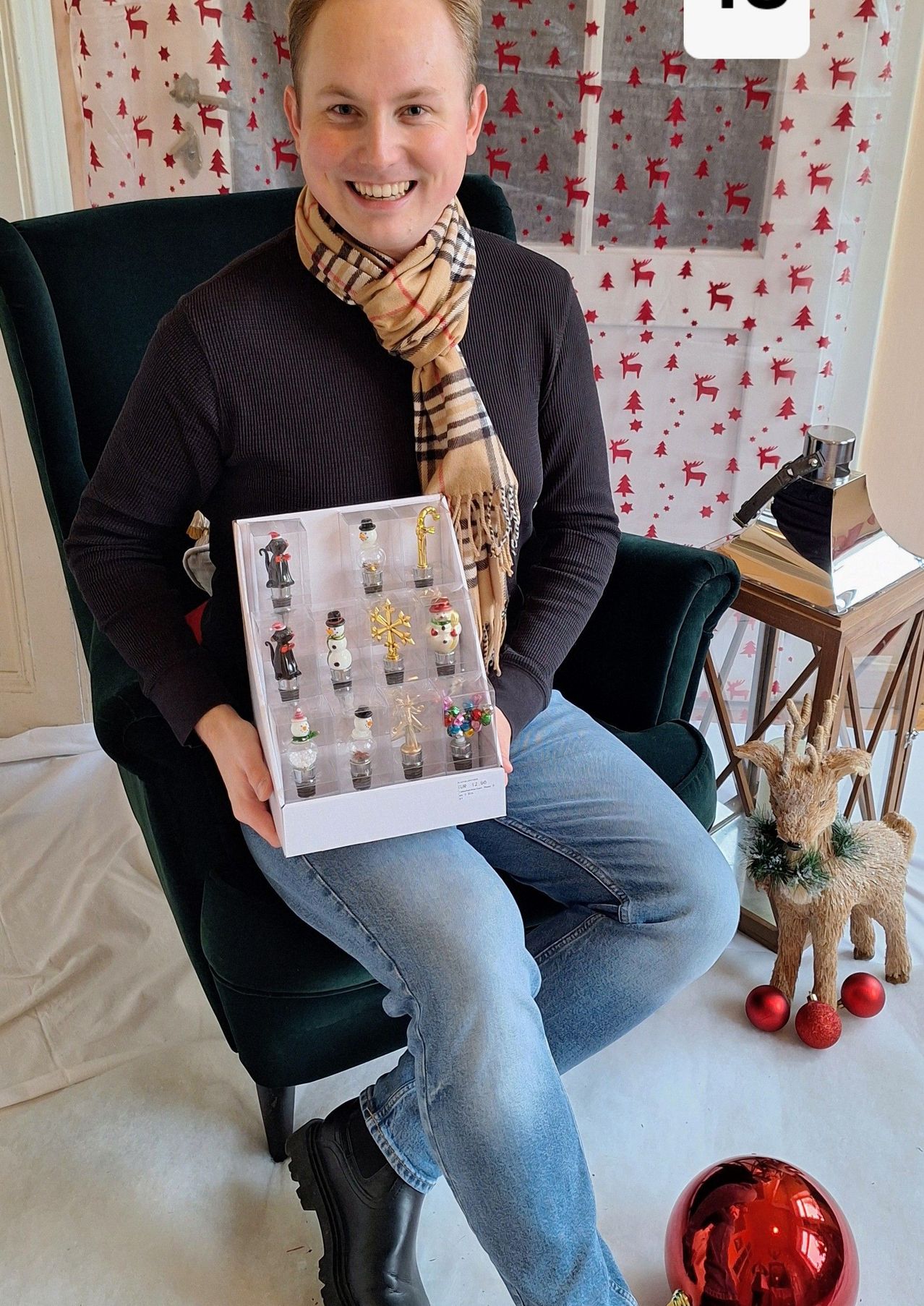 Eine Person mit Schal hält eine Schachtel mit Weihnachtsschmuck in einem festlich dekorierten Raum.