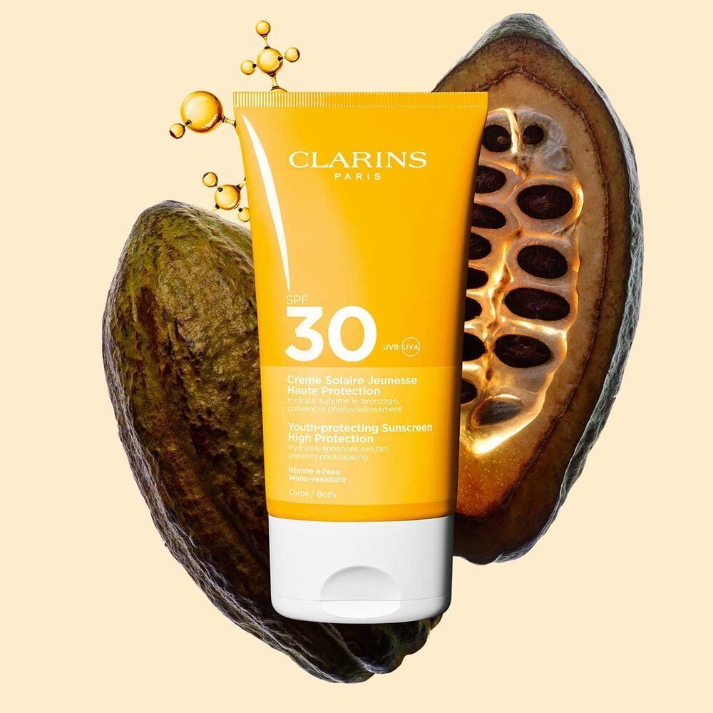 A tube of Clarins SPF 30 sunscreen with cocoa pods in the background, highlighting its youth-protecting properties and hydration benefits.