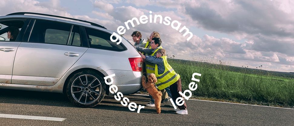 Drei Menschen in Warnwesten schieben ein silbernes Auto am Straßenrand, begleitet von einem braunen Hund. Die Worte 'Gemeinsam besser leben' sind prominent angezeigt.