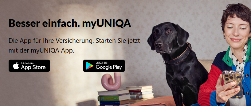 Eine Frau in einem bunten Pullover sitzt auf einem Sofa, lächelt, mit zwei schwarzen Labradoren. Ein Hund trägt ein Halsband, und Bücher und ein rosa Objekt sind auf dem Tisch.