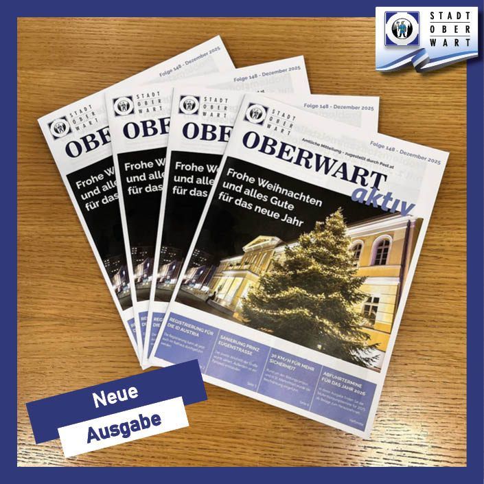 Mehrere Ausgaben einer Zeitschrift mit dem Titel 'Oberwart aktuell' sind auf einer Holzoberfläche zu sehen. Die Titelbilder zeigen einen festlichen Weihnachtsbaum vor einem Gebäude mit leuchtenden Fenstern.