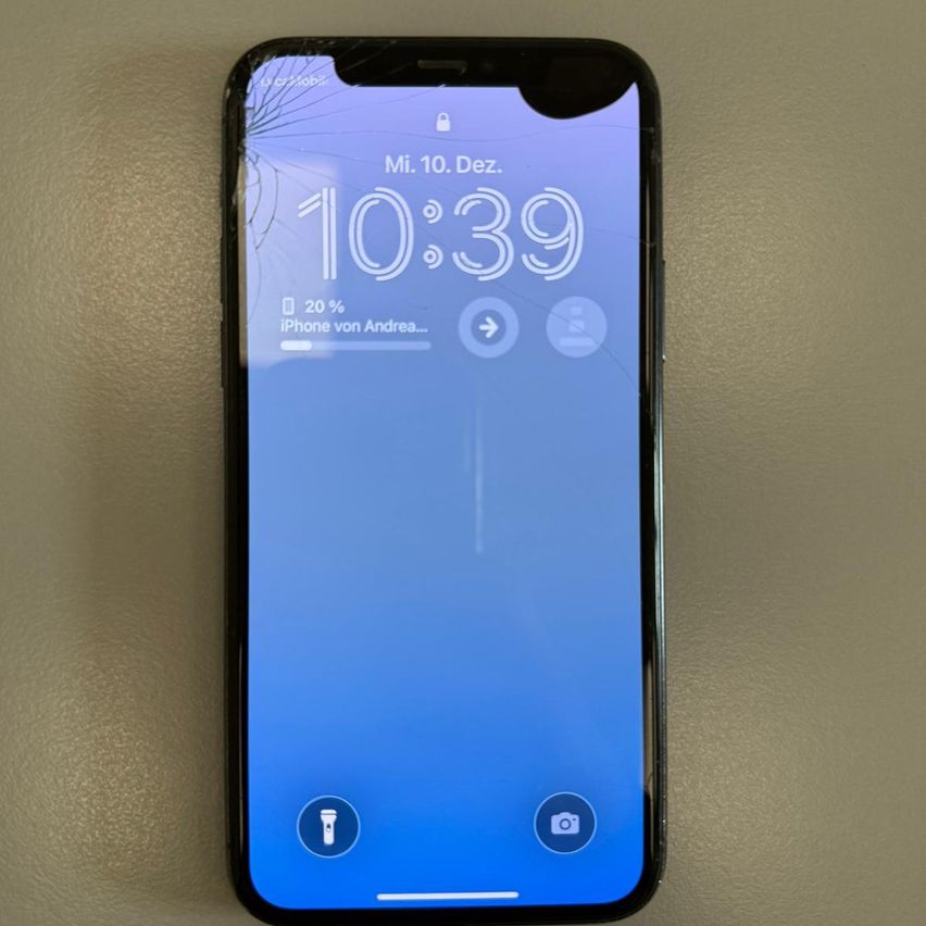 Ein Smartphone mit einem gebrochenen Bildschirm wird vor einem beigefarbenen Hintergrund gezeigt. Die Zeit auf dem Bildschirm zeigt 10:39. Der Bildschirm zeigt 20% Akkuladung.